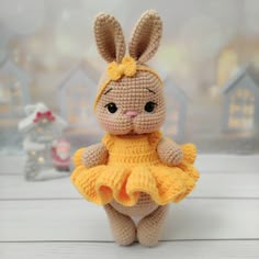 a crocheted bunny doll in a yellow dress on a white table next to small houses