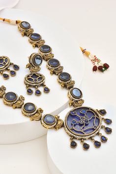 This Zirconia Kundan Necklace set is a perfect fusion of classic craftsmanship and modern elegance. Featuring vibrant blue zirconia stones set in traditional Kundan work, this necklace is finished with a gleaming gold polish, making it a standout piece for any occasion. Paired with matching earrings, this set is an ideal choice for weddings, festive celebrations, or a statement look. Festive Necklaces With Stone Setting, Temple Jewelry Sets With Round Stone Setting, Round American Diamond Temple Jewelry Necklace, Festive Round Temple Necklace With Hand Set, Festive Round Gemstone Bridal Necklace, Festive Hand Set Round Temple Necklace, Festive Bridal Necklace With Gemstones, Festive Round Bridal Necklace With Gemstone, Festive Bridal Gemstone Necklace