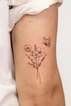 a small flower tattoo on the side of a woman's right leg, with two butterflies flying over it