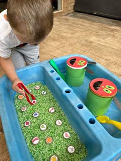 a young boy playing in a sand and water tray with green sprinkles