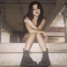 a woman sitting on some steps with her legs crossed and wearing black boots, looking at the camera