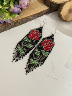 two pairs of beaded earrings with red roses on them sitting on a table next to flowers