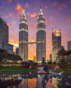 there are two very tall buildings in the city at sunset or dawn, and one is reflecting on the water