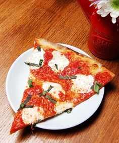 two slices of pizza sitting on top of a white plate next to a vase with flowers