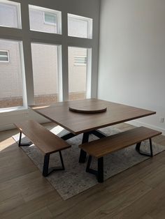 a wooden table with two benches in front of large windows and hardwood flooring area