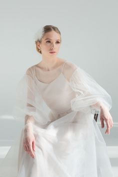 a woman in a white dress sitting on a chair with her hands behind her back