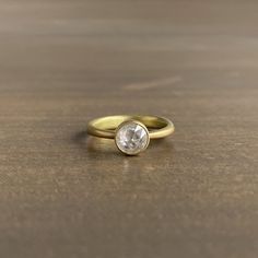 a yellow gold ring with an oval shaped diamond on the center, sitting on a wooden surface