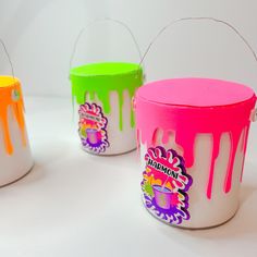 three buckets with different colors and designs painted on the side, one is pink, one is green