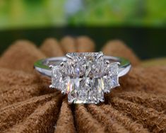 a cushion cut diamond ring sitting on top of a pile of brown fabric with a green background