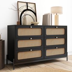 a black dresser with wicker drawers in a white walled living room next to a lamp