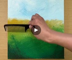 a person holding a comb in front of a painting with green and yellow paint on it