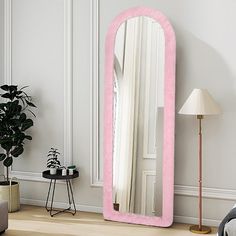 a large pink mirror sitting on top of a wooden floor next to a chair and lamp