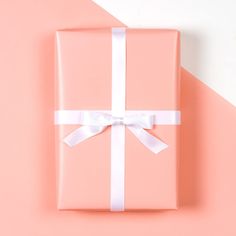 a pink gift box with a white ribbon and bow on an orange and pink background