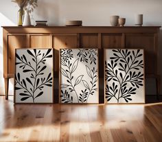 three black and white paintings sitting on top of a wooden floor next to a shelf