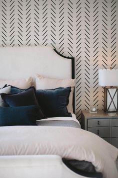 a white bed topped with lots of pillows next to a night stand and nightstands