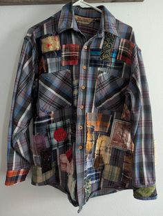 a shirt that is hanging up on a wall with buttons and patchwork designs all over it