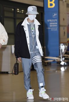 a man wearing a white hat and grey sweatpants is walking through an airport terminal