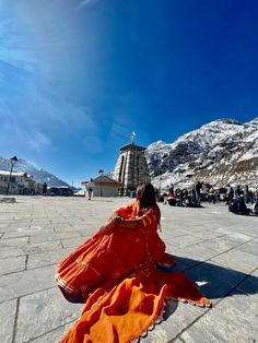 a woman in an orange dress sitting on the ground and looking up into the sky