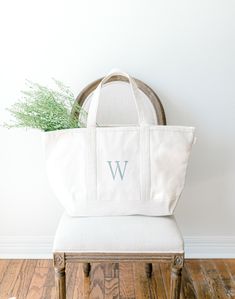 a white tote bag sitting on top of a wooden chair next to a plant