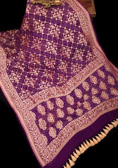 Indulge in a captivating journey that takes you from Banaras, Uttar Pradesh to Kutch, Gujarat with this exquisite saree. Meticulously crafted using the traditional Bandhej technique, it features Shikaargah motifs, beautifully adorned with a jaal pattern. The saree's body boasts of stunning zari elephant, peacock, parrot, and camel motifs alongside intricate floral vines. The border is embellished with elephant and peacock motifs, lending an air of luxury to the ensemble. The resist-dyed dots on the jaal are hand-plucked, showcasing the artisan's formidable skills. The saree's pallu is a veritable masterpiece, featuring elements of the Shikaargah theme, such as an elephant and twin parrot, woven in pure Banarasi Silk Georgette fabric in a rich purple hue. This exclusive piece is an ode to t Kutch Gujarat, Peacock Motifs, Saree Blouses, Rich Purple, Georgette Saree, Purple Silk, Georgette Fabric, Floral Vine, Uttar Pradesh