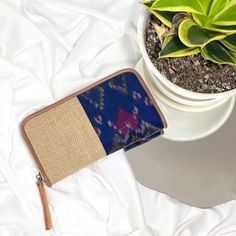 a purse sitting on top of a white bed next to a potted plant with green leaves