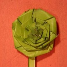 an origami flower sitting on top of a green stick in front of a red wall