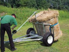 a man is pushing a cart with hay on it in the grass and another person standing next to it