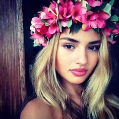 a woman with long blonde hair wearing a pink flower crown on her head and looking at the camera