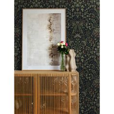 a vase with flowers sitting on top of a wooden cabinet in front of a wallpapered wall