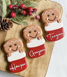 three decorated cookies sitting on top of a wooden cutting board next to pine cones and berries