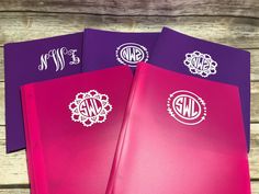 three personalized notebooks with monogrammed stickers on the covers, one pink and one purple