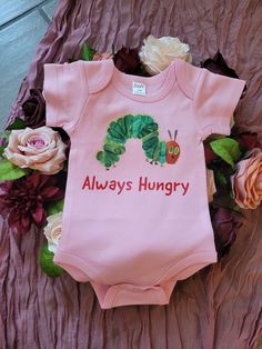 "This baby bodysuit is inspired by the book A Very Hungry Caterpillar written by Eric Carle. You can personalize the words at no extra charge. This is a great shirt to be personalized for a 1st birthday party.  The shirt will say \"Always Hungry\" unless personalization is requested. The product is 100% cotton and very comfortable. The fabric is completely opaque and are machine washable." Fitted Pink Bodysuit With Cartoon Print, Cute Short Sleeve Onesie For First Birthday, Fitted Cartoon Print Bodysuit For Playtime, Fitted Short Sleeve Cotton Bodysuit With Cartoon Print, Cute Fitted Bodysuit With Cartoon Print, Customizable Fitted Onesie For First Birthday, Fitted Onesie With Cartoon Print For Spring, Pink Character Print Onesie For Playtime, Cute Cotton Bodysuit With Character Print