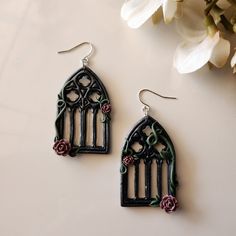 a pair of earrings with flowers on them sitting next to a white flower vase and some petals