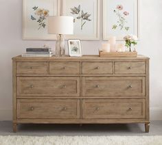 a dresser with flowers and candles on it in front of two framed pictures hanging on the wall