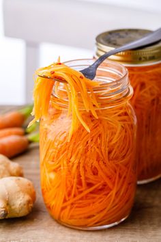 carrots and ginger paste in jars on a wooden table with fresh cut up root vegetables