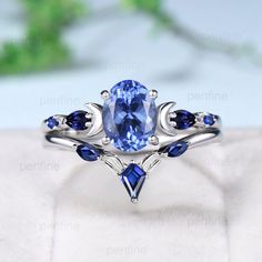 a ring with blue sapphire stones and leaves on the side, sitting on top of a white