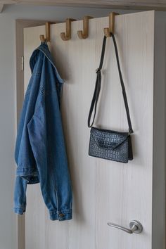 a denim jacket hanging on the wall next to a purse and coat rack with hooks