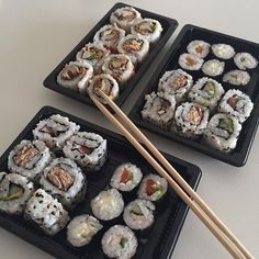 two trays with sushi and chopsticks on them