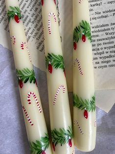 three white candles with holly and candy canes on them next to an open book