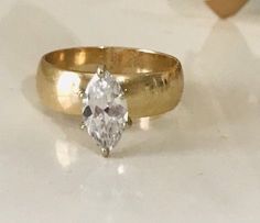 a gold ring with a pear shaped diamond in the center on a white table top