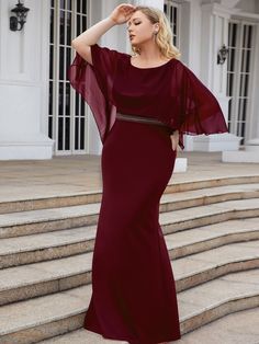 a woman in a long red dress standing on steps with her hands behind her head