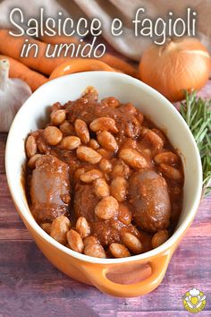 a bowl filled with beans and meat on top of a wooden table next to carrots