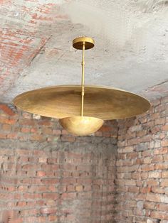 a large brass light fixture hanging from the ceiling in an old brick room with exposed ceilings