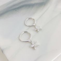 This is a pair of dainty huggie earrings which are made from 925 sterling silver and which feature a small pendant with five, clear-coloured, Marquise zircon stones arranged in a flower shape hanging from the lower edge of the hoop. They fasten with a hinge clasp (also on the lower edge of the hoop), and have a thin earpiece which threads through the earlobe. This is a delicate and elegant pair of earrings that will add a classy touch of sparkle to any outfit.  Packaging: Beautifully packed in a box, ready for gifting. Details: ✅ Material: 925 sterling silver ✅ Diameter: hoop diameter: 1.1 cm ✅ Charm size: 7.5 mm ✅ Weight: 3.0 g 🏷️ This product is made of sterling silver -- easily recognizable by its '925' stamp of authenticity. It is also hypoallergenic, making it suitable for people wit Hoops With Charms, Earrings Flower, Jewelry Lookbook, Sterling Silver Hoop Earrings, Huggie Earrings, Small Pendant, Huggie Hoop Earrings, Sterling Silver Hoops, Flower Charm