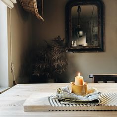 a lit candle sitting on top of a wooden table next to a mirror and potted plant