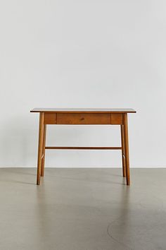 a small wooden table sitting on top of a cement floor next to a white wall