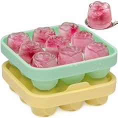 an ice cube tray filled with pink and green frozen drinks next to a plastic scooper