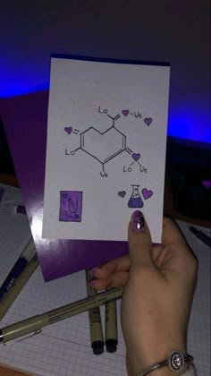 someone is holding up a card with the chemical symbol for love on it and some pens next to it