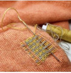 an orange sweater with yellow and gray stitching next to a pair of knitting needles