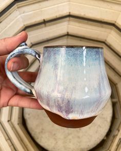 a hand holding a blue and white coffee mug in front of a wall with an arch